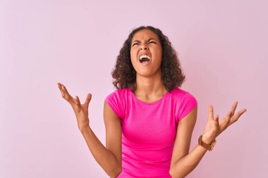Genç Brezilyalı kadın izole pembe arka plan üzerinde ayakta t-shirt giyen çılgın ve deli çığlık ve agresif ifade ve kollar ile bağırdı kaldırdı. Hayal kırıklığı kavramı.