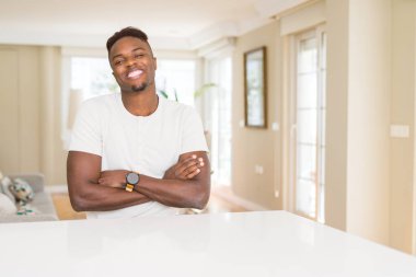 Beyaz masada yakışıklı Afrikalı Amerikalı adam evde mutlu yüz kamera bakarak çapraz silah ile gülümsüyor. Pozitif kişi.