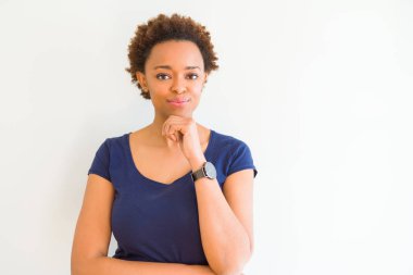 Emin çapraz kollar ve çeneme kaldırdı el ile gülümseme ile kameraya bakarak beyaz arka plan üzerinde genç güzel Afrikalı-Amerikalı kadın. Pozitif düşünce.