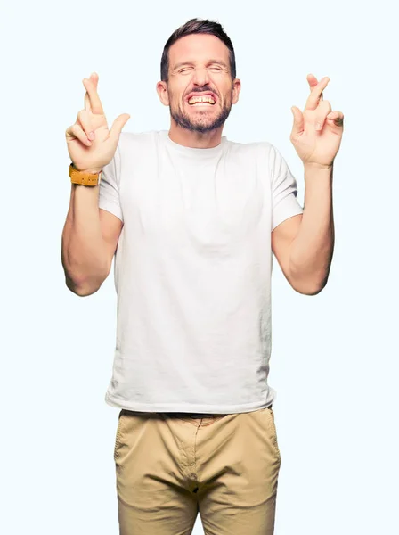 Bonito Homem Vestindo Camiseta Branca Casual Sorrindo Cruzando Dedos Com — Fotografia de Stock