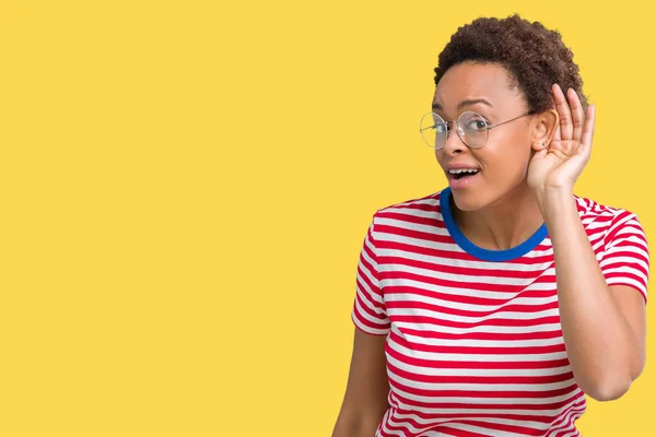 Beautiful young african american woman wearing glasses over isolated background smiling with hand over ear listening an hearing to rumor or gossip. Deafness concept.