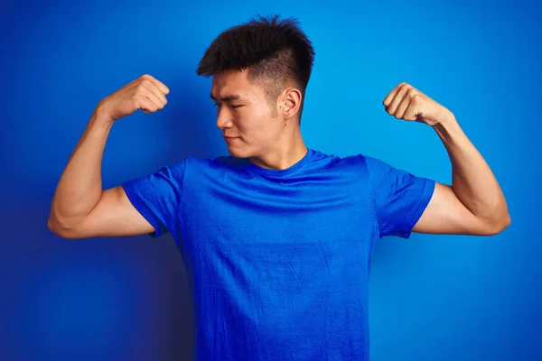 孤立した青い背景の上に立つTシャツを着た若いアジア人の中国人男性は 腕の筋肉が誇らしげに微笑んでいる フィットネスコンセプト — ストック写真
