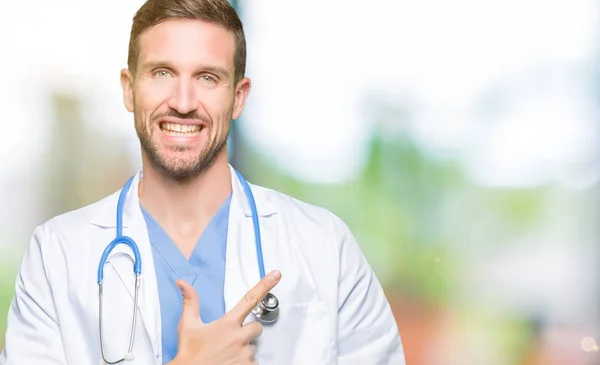 帅气的医生在孤立的背景下穿着医疗制服 愉快地微笑着用手和手指指着一边 脸上带着快乐和自然的表情 — 图库照片