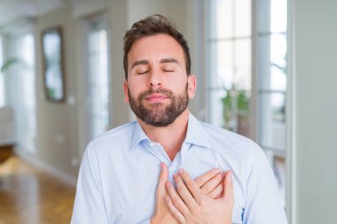 Yakışıklı iş adamı kapalı gözleri ve yüzünde minnettar jest ile göğüs elleri ile gülümseyen. Sağlık kavramı.