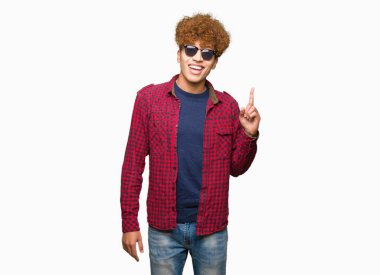 Yakışıklı genç afro saçlı başarılı fikirle parmak işaret güneş gözlüğü takıyor. Çıktıktan ve mutlu. Bir numara.