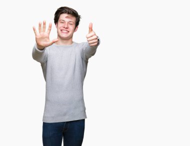 Gösterilen arka plan üzerinde kış kazak giyen genç yakışıklı adam izole ve parmakları ile işaret kendinden emin ve mutlu gülümseyerek süre 6 numara.