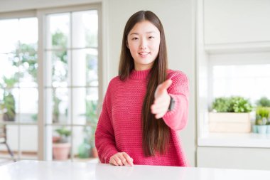 Beyaz masada pembe kazak giyen güzel Asyalı kadın tebrik ve davetkar olarak dostu sunan el sıkışması gülümseyen. Başarılı iş.