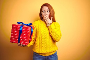 Genç Güzel Redhead kadın tutan Doğum günü hediyesi sarı izole arka plan kapağı ağız üzerinde hata için utanç ile şok, korku ifadesi, sessizlik korkuyor, gizli kavramı