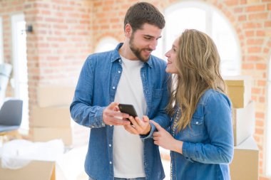 Genç çift karton kutular etrafında akıllı telefon kullanarak yeni bir eve hareket