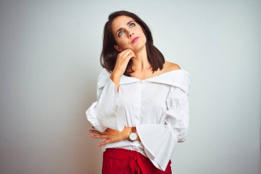 Genç güzel kadın t-shirt üzerinde ayakta beyaz izole arka plan üzerinde el çene üzerinde soru hakkında düşünme, dalgın ifade. Düşünceli bir yüz ile gülümsüyor. Şüphe kavramı.