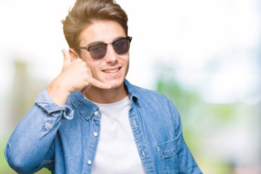 Yakışıklı delikanlı yapıyor gülümseyen izole arka plan üzerinde güneş gözlüğü takıyor telefon hareketi ile el ve parmak telefonda konuşuyor gibi. Kavramları iletişim.