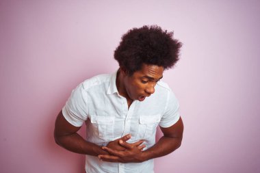 Afro saç ile genç Amerikalı adam beyaz gömlek ayakta mide el ile izole pembe arka plan üzerinde dikili çünkü hazımsızlık, ağrılı hastalık duygusunu. Ağrı kavramı.