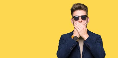 Genç yakışıklı zarif adam ağız hata için elleriyle kapsayan şok güneş gözlüğü takıyor. Gizli kavramı.