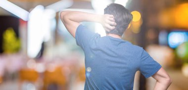 İzole arka plan geriye düşünme hakkında şüphe ile baş taraftan üzerinde mavi t-shirt giyen genç yakışıklı adam