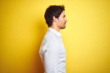 Genç yakışıklı işadamı, izole sarı arka planda ayakta duran zarif gömlek giyen yan bakmak, güvenli bir gülümseme ile doğal yüz ile profil poz rahatlayın.