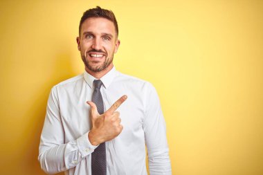 Yüze mutlu ve doğal ifade ile yan kadar el ve parmak ile işaret yüz bir gülümseme ile neşeli sarı izole arka plan üzerinde zarif beyaz gömlek giyen genç yakışıklı iş adamı