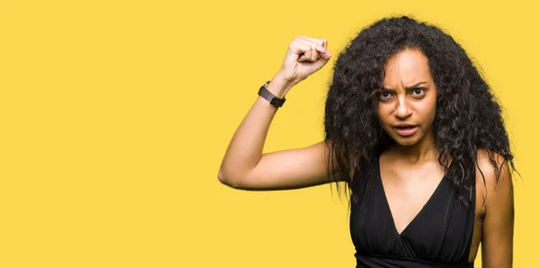 Young beautiful girl with curly hair wearing fashion skirt angry and mad raising fist frustrated and furious while shouting with anger. Rage and aggressive concept.