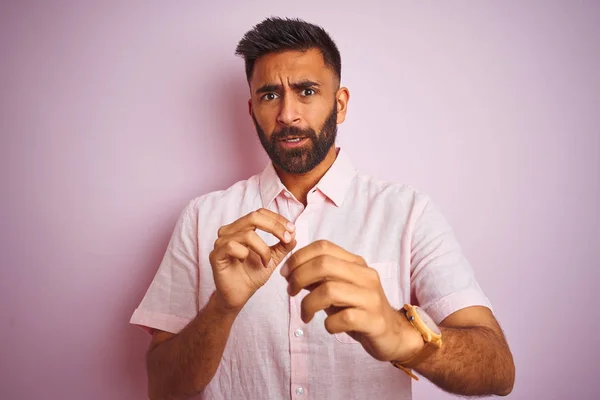 Young indian man wearing casual shirt standing over isolated pink background disgusted expression, displeased and fearful doing disgust face because aversion reaction. With hands raised. Annoying concept.
