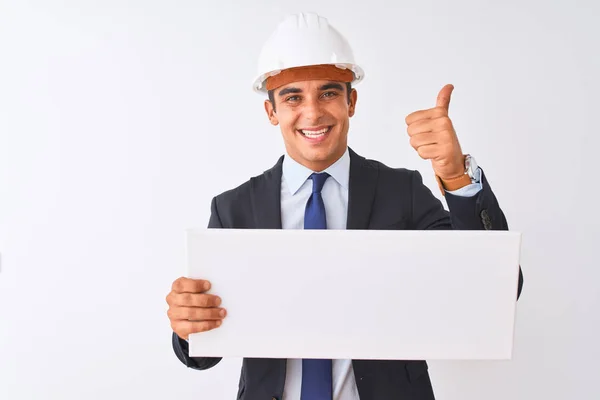 年轻的英俊建筑师男子戴着头盔举着横幅在孤立的白色背景高兴与大微笑做Ok标志 拇指用手指 优秀的标志 — 图库照片