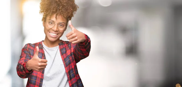 美丽的年轻非洲裔美国妇女戴眼镜在孤立的背景下 批准做积极的手势与手 竖起大拇指微笑 并为成功高兴 看着镜头 赢家的手势 — 图库照片