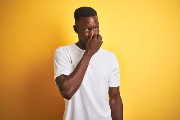 孤立した黄色の背景の上に立つ白いTシャツを着た若いアフリカ系アメリカ人男性は 鼻に指で息を止め 耐えきれない匂いを嗅ぐ 悪臭の概念 — ストック写真