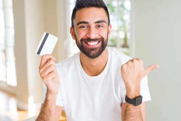 Hombre Hispano Guapo Sosteniendo Tarjeta Crédito Señalando Mostrando Con Pulgar —  Fotos de Stock