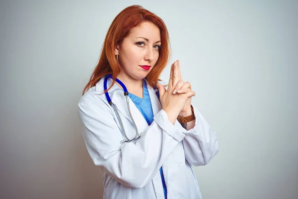 Young redhead doctor woman using stethoscope over white isolated background Holding symbolic gun with hand gesture, playing killing shooting weapons, angry face
