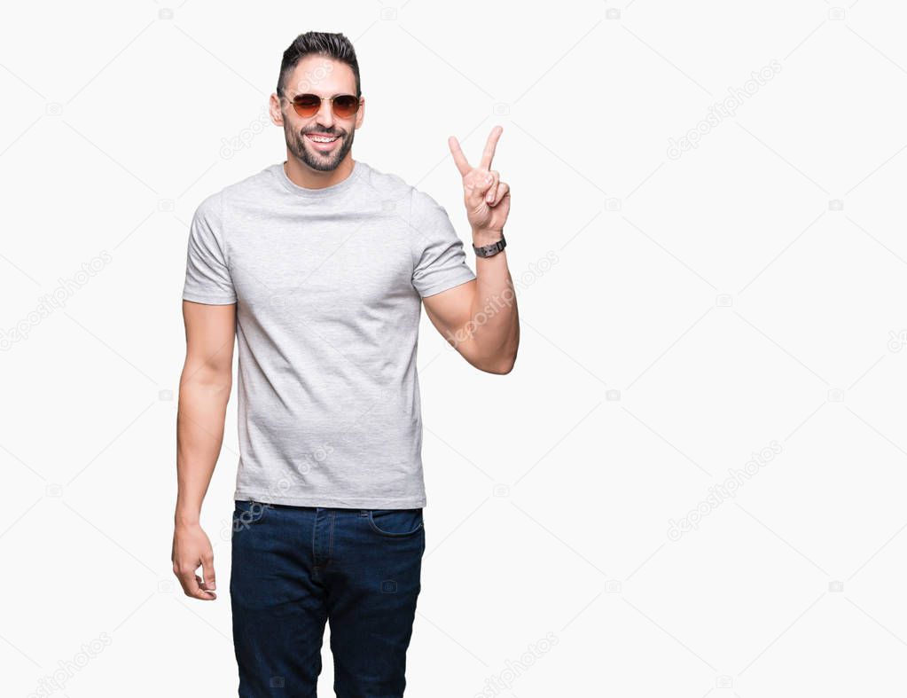 Young handsome man wearing sunglasses over isolated background smiling with happy face winking at the camera doing victory sign. Number two.