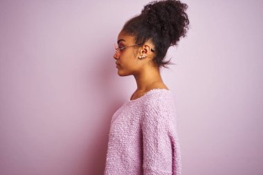 Afrika Amerikan kadın yan arıyor izole pembe arka plan üzerinde kış kazak ve güneş gözlüğü giyen, güvenli bir gülümseme ile doğal yüzü ile profil poz rahatlayın.