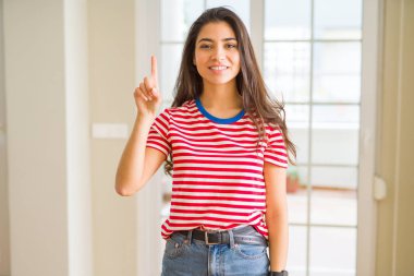 Genç güzel kadın giyiyor rahat t-shirt gösterme ve kendinden emin ve mutlu gülümseyen bir parmak ile işaret eden oktan yukarı.