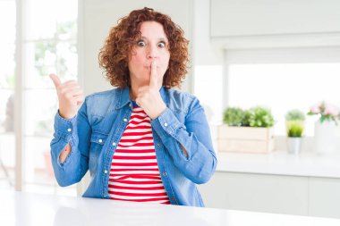 Evde kot ceket giyen kıvırcık saçlı orta yaş yaşlı kadın yan el ile işaret dudaklarında parmak ile sessiz olmak isteyen. Sessizlik ve gizli kavram.