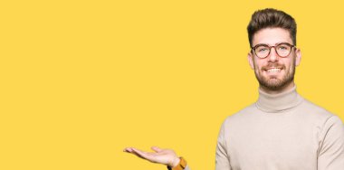 Hayret ve el ile sunulması ve parmak ile işaret ederken kameraya gülümseyen gözlüklü genç yakışıklı iş adamı.