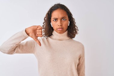 Brezilyalı kadın öfkeli yüzü ile izole beyaz arka plan üzerinde kablosuz kulaklıklar kullanarak müzik dinleme, negatif işareti başparmak aşağı ile sevmediğim gösteren, ret kavramı