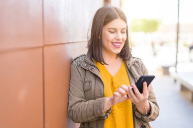 Güzel genç kadın gülümseyen pozitif kullanarak smarpthone eğilme 