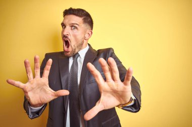 Sarı izole arka plan üzerinde genç yakışıklı iş adamı korkuyor ve korku ifadesi ile korkuyor el ile hareket durdurmak, şok bağırıyor. Panik konsepti.