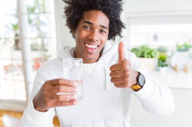 Afrikalı Amerikan adam evde bir bardak su içme büyük gülümseme ile ok işareti, parmaklar yukarı başparmak, mükemmel işareti yapıyor mutlu