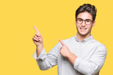 Gülümseyen ve iki elleri ve parmakları ile tarafına işaret kamera bakarak izole arka plan üzerinde gözlük takan genç yakışıklı adam.