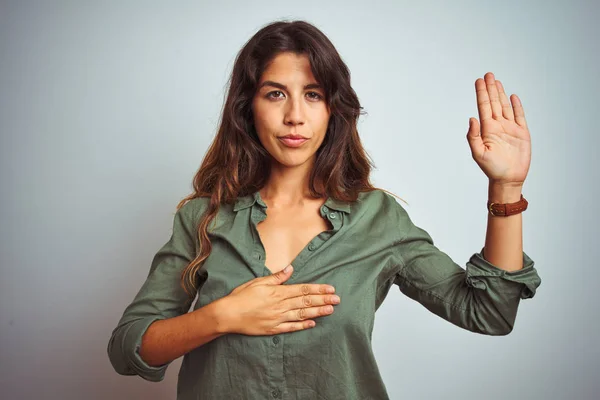 Young beautiful woman wearing green shirt standing over grey isolated background Swearing with hand on chest and open palm, making a loyalty promise oath