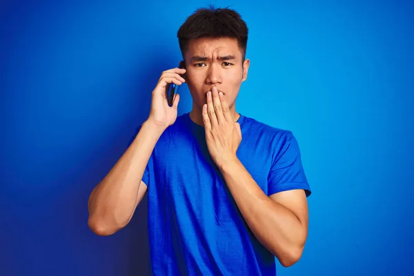 年轻的亚洲中国男子在智能手机上说话站在孤立的蓝色背景盖嘴与手震惊与耻辱的错误 表达恐惧 害怕在沉默 秘密概念 — 图库照片