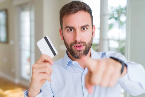 Handsome business man holding credit card pointing with finger to the camera and to you, hand sign, positive and confident gesture from the front