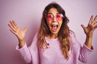 Pembe izole arka plan üzerinde ayakta moda güneş gözlüğü giyen genç güzel kadın deli kutluyor ve başarı için hayran silah kaldırdı ve açık gözleri heyecanlı çığlık. Kazanan kavramı
