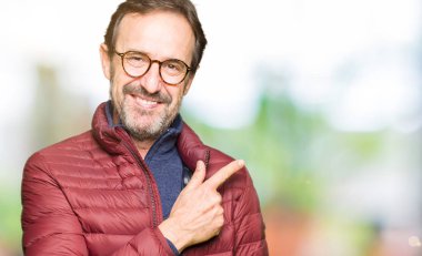 Orta yaş yakışıklı adam gözlük ve kış ceket neşeli bir gülümseme ile el ve parmak kadar yan yüzünde mutlu ve doğal ifade ile işaret eden yüz