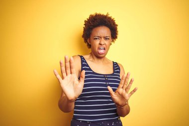 Beauitul Afrikalı Amerikan kadın izole sarı arka plan üzerinde yaz t-shirt giyiyor korkuyor ve korku ifadesi ile korkmuş el ile jest durdurmak, şok bağırıyor. Panik konsepti.