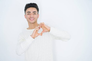 Beyaz izole arka plan üzerinde yakışıklı genç adam sevgi gösteren kalp sembolü ve elleri ile şekil gülümsüyor. Romantik konsept.