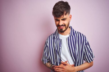 Dövme ile genç adam izole pembe arka plan üzerinde duran çizgili gömlek ayakta karnında el ile çünkü hazımsızlık, ağrılı hastalık duygusunu. Ağrı kavramı.