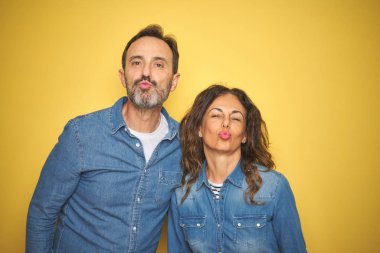 Güzel ve seksi olmak havada bir öpücük üfleme kamera bakıyor izole sarı arka plan üzerinde ayakta birlikte hoş orta yaş çift. Aşk ifadesi.