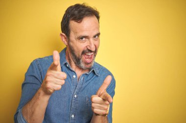 Sarı arka plan üzerinde gri saçlı yakışıklı Orta Çağ kıdemli adam parmak kamera mutlu ve komik yüz ile işaret ediyor. İyi enerji ve Vibes.