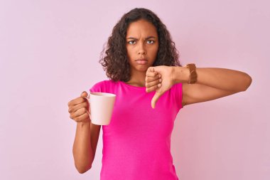 Genç Brezilyalı kadın kızgın yüz ile izole pembe arka plan üzerinde ayakta kahve bardak içme, negatif işareti başparmak aşağı ile sevmediğim gösteren, ret kavramı