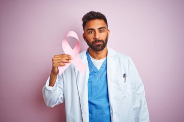 Genç Hint Doktor adam tutan kanser şerit ayakta üzerinde sağlam bir ifade ile izole pembe arka plan üzerinde akıllı yüz düşünme ciddi