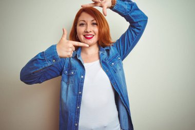 Beyaz izole arka plan üzerinde ayakta kot gömlek giyen genç güzel Redhead kadın mutlu yüz ile eller ve parmaklar ile çerçeve yapma. Yaratıcılık ve Fotoğrafçılık konsepti.